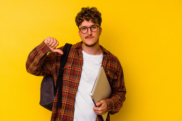 Young student caucasian man holding a laptop isolated on yellow background showing a dislike gesture, thumbs down. Disagreement concept.
