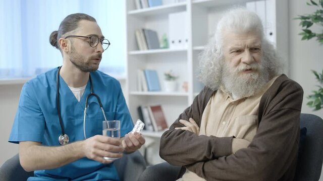 Senior patient refusing to take pills, nurse taking care of pensioner at home