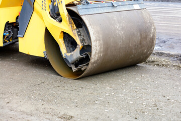 A massive metal cylinder of a road roller compacts sandy substrates at a construction site. Close-up.