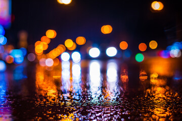 Rainy night in the city. Headlights approaching cars. Reflections of street lamps on the wet asphalt. Colorful colors. Close up view from the asphalt level.