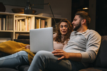 couple relaxing on sofa at home using laptop