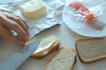 Man spreads butter on a piece of wheat bread using knife doing sandwich with red fish for breakfast, hands closeup. Preparing food at home concept. Fast food nutrition.