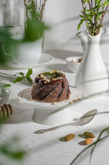 Brownie cake poured with chocolate and nuts on a white stand