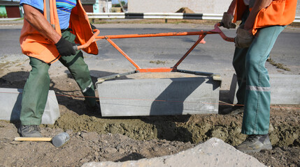 Workers install a curb in concrete, construction of a pedestrian road.