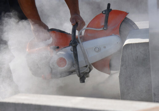 A construction worker saws a large concrete block with a circular saw,close-up.