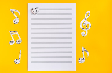 Blank sheet music, music notes and hearts cut from music text on yellow background. Top view