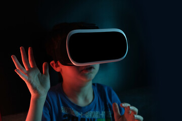 boy, child in dark room with neon lights in modern VR glasses interacting with network while having virtual reality experience, concept study of another world, modern teaching technologies