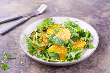 Diet vegetarian vitamin salad of orange pieces and mix of arugula, chard and mizun leaves on a plate on the table