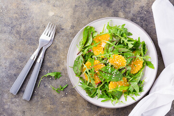 Diet vegetarian vitamin salad of orange pieces and mix of arugula, chard and mizun leaves on a plate on the table. Top view