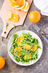 Diet vegetarian vitamin salad of orange slices and a mix of arugula, chard and mizun leaves on a plate and a cutting board with peeled orange on the table. Top and vertical view