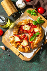 Healthy pastries gluten free, made from rye flour, diet food. Galette tomatoes, mozzarella and basil on a stone background. Top view, flat lay. Copy space.