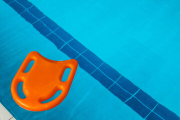 a board with swimming handles lies on the surface of the water in the swimming pool. swimming board