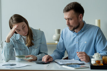 Young married couple sitting at living room table, studying papers, makes calculations on a calculator, studies the family budget