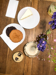 New York cheesecake, peanut butter cookie, chocolate cookie, and ice coffee on a wooden table with a flower in a cafe. Top view.