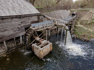 Fototapeta na wymiar Water mill wheel rotates under a stream of water. Traditional village machinery