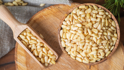 Fototapeta na wymiar Round bowl with peeled pine nuts, scoop with nuts on the background of a round wooden board.