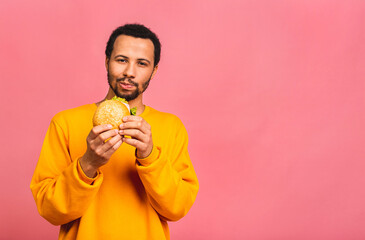 Young african american black man eating hamburger isolated over pink background. Diet concept.