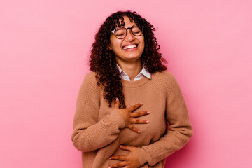 Young mixed race woman isolated on pink background laughs happily and has fun keeping hands on...
