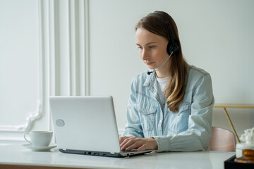 Female talking in a video conference on line with a headset with microphone and using laptop in office, consulting client