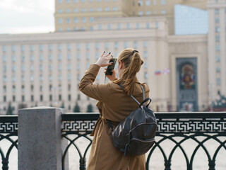 People in the public park in spring day. Leisure theme. Young woman taking photography of the Moscow cityscape.  Back, rear view.
