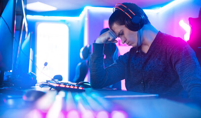 Streamer young man facepalm professional gamer playing online games computer with headphones, neon...