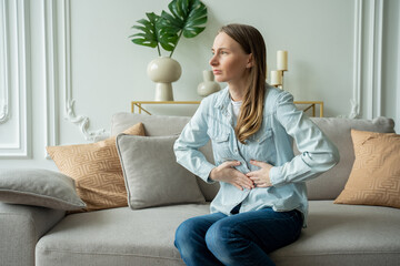 Young woman suffering from abdominal pain while sitting on sofa at home