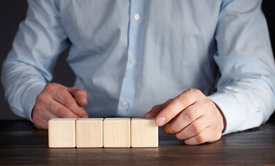 Wooden cubes on the table. Male businessman with hand puts the cube in a row.