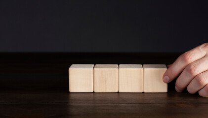 Wooden cubes on the table. The hand puts the cube in a row.