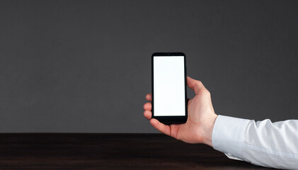 Phone in hand on a dark background. Businessman in shirt. Blank white screen.