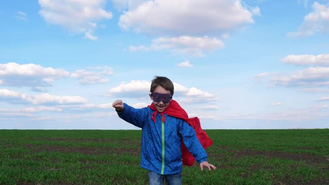 A happy boy in a red raincoat runs across a meadow against a blue sky. The child depicts a cartoon style. Funny cartoon superhero character. The concept of leadership.