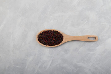 Black quinoa seeds in wooden spoon, top view. Healthy cereals contain a large amount of protein, antioxidants, dietary fiber, vitamins and minerals. Gray background, copy space