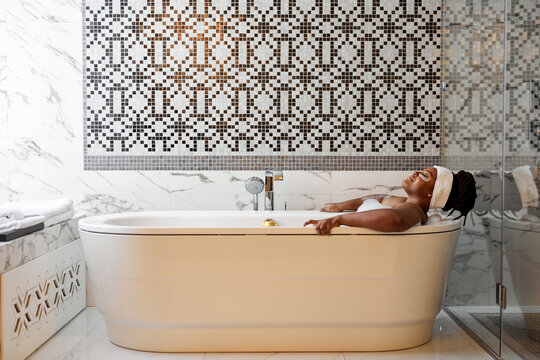 Relaxed african woman taking bath with foam with pleasure, enjoying spa, hygiene