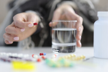 Female hands hold pill and glass of water.