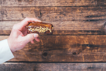 Man's hand holds eclair on a wooden background.