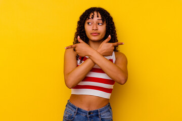 Young mixed race woman isolated on yellow background points sideways, is trying to choose between two options.