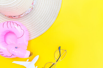 Summer beach composition. Minimal simple flat lay with plane sunglasses hat and Inflatable flamingo isolated on yellow background. Vacation travel adventure trip concept. Top view copy space.