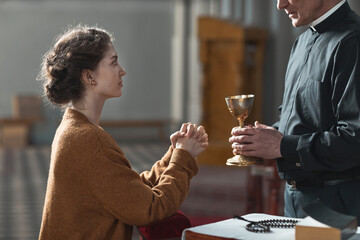 Faithful woman sitting in front of the priest and praying while he holding the cup