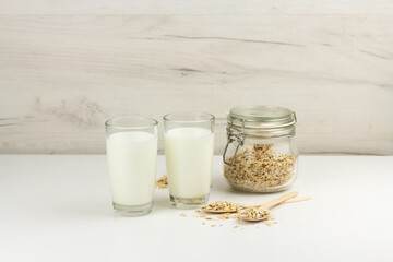 Dairy free oat milk i glasses and flakes in a glass jar on light background