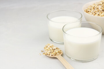 Dairy free oat milk in glasses and flakes on light background