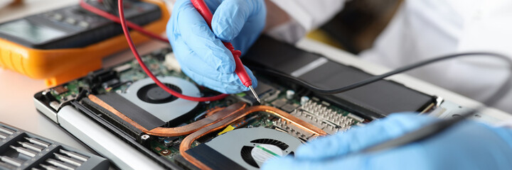 Professional repairman holding red tester in rubber gloves over laptop closeup