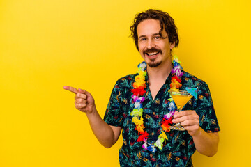 Young caucasian man wearing a hawaiian necklace holding a cocktail isolated on yellow background...