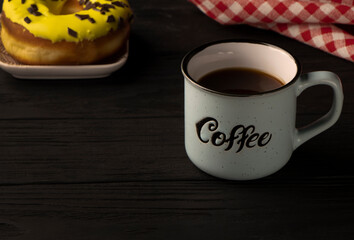 coffee time. A cup with the inscription stands on a black wooden background. Donut with pink icing on the back. High quality photo