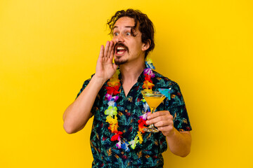 Young caucasian man wearing a hawaiian necklace holding a cocktail isolated on yellow background shouting and holding palm near opened mouth.