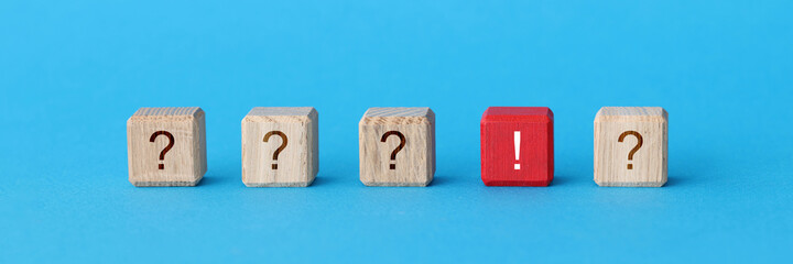 Red wooden cube with exclamation mark lying among cubes with question marks closeup