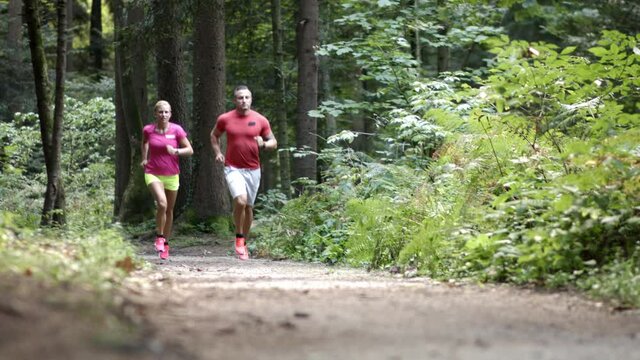 Wide shot of Caucasian couple in sportswear, running along a forest trail