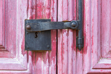 Detail of pink door with antique cast iron lock and worn paint marking a vintage style