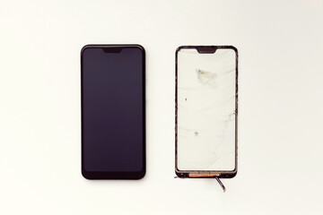 Repair and replacement of a mobile phone touchscreen. Refurbished smartphone and non-working touchscreen on a white background. View from above.