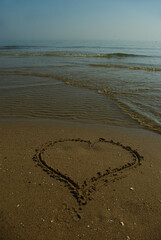 
In the foreground a heart drawn on the sand of a beach.