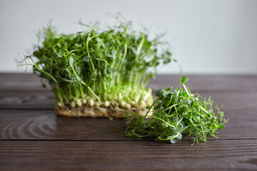 Pea microgreens, young green shoots on brown wooden table. Cutted micro greens with fresh leaves on grey