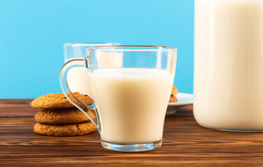 A jug and a glass of milk on a wooden table, on a blue background.